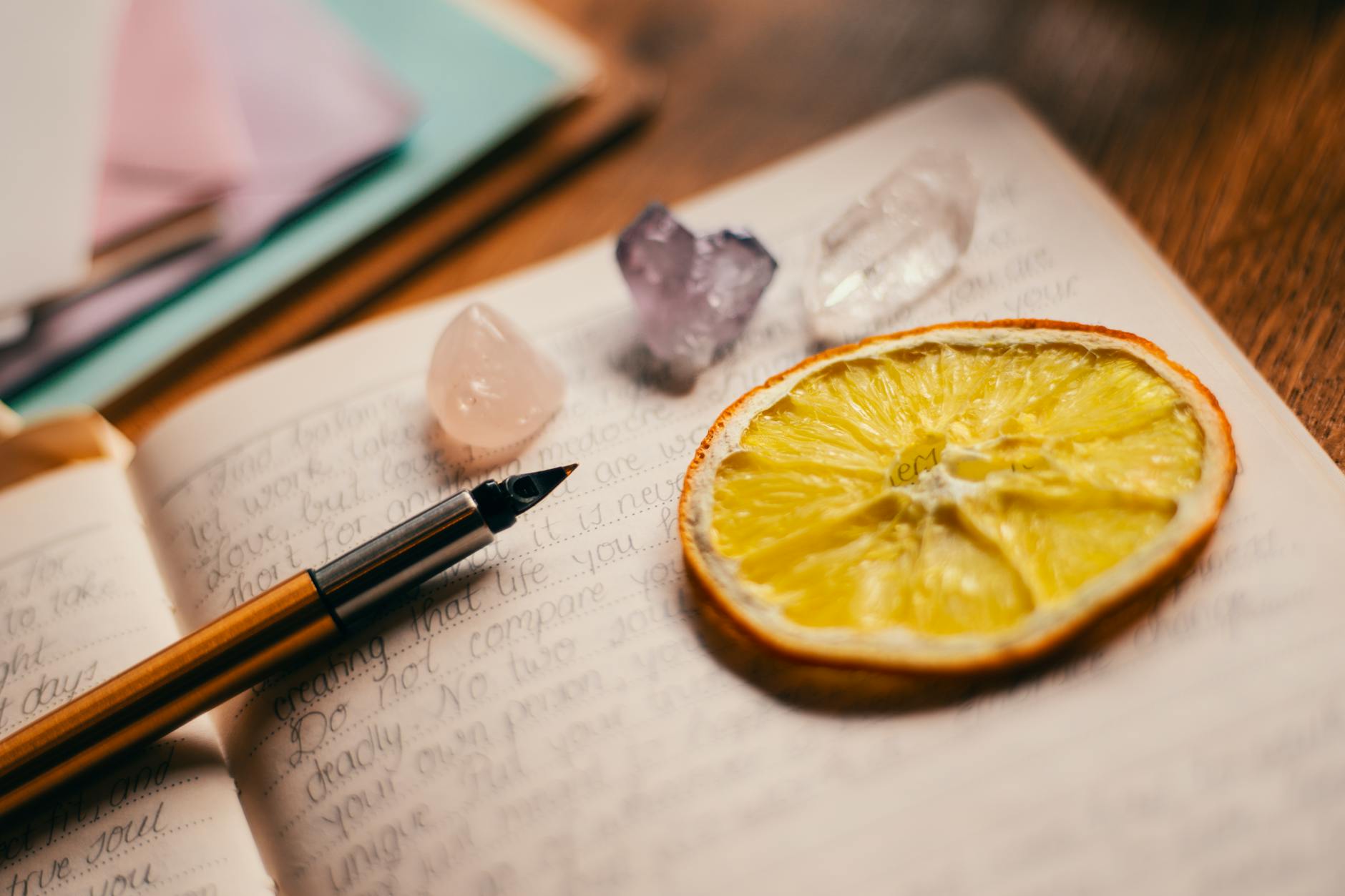 A journal, pen, crystals, and an orange slice coaster lie on a table.