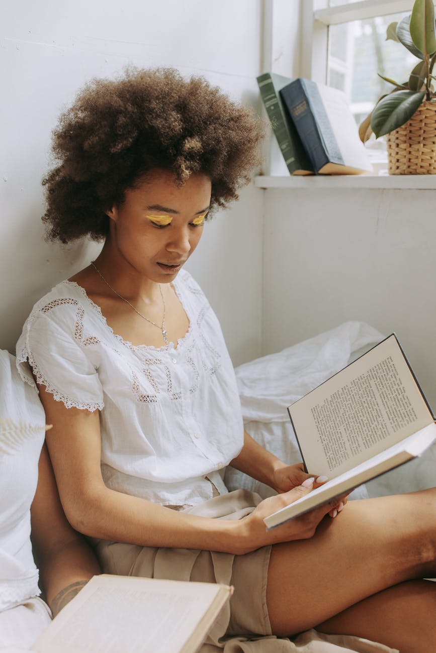 A girl reads a book in bed.

