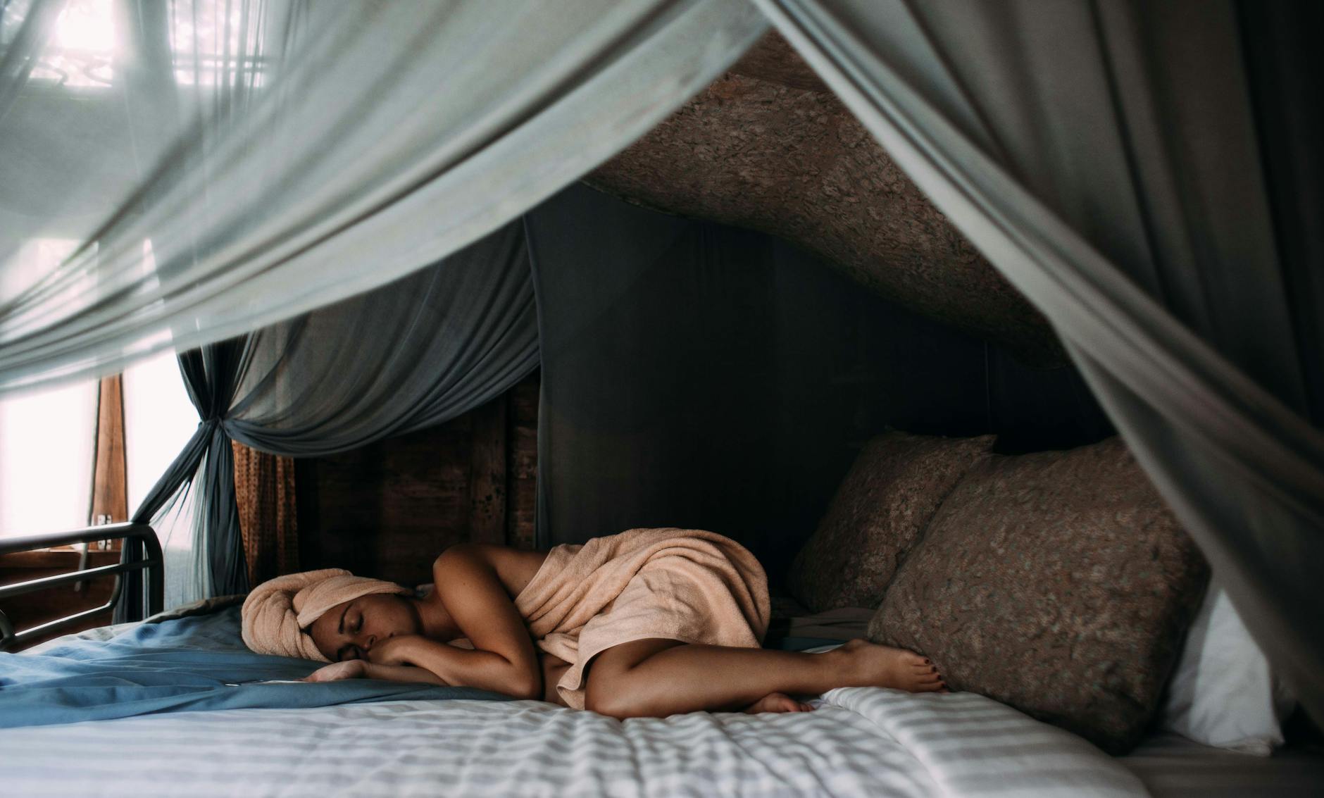 A person sleeps under a canopy in bed.
