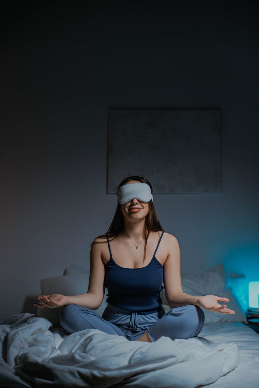 A woman meditates in bed
with a sleep mask over her eyes.