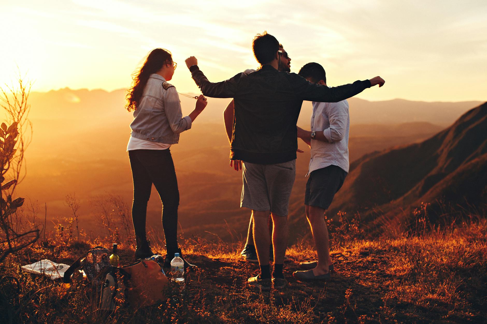 Four people gather in the mountains by a setting sun.
