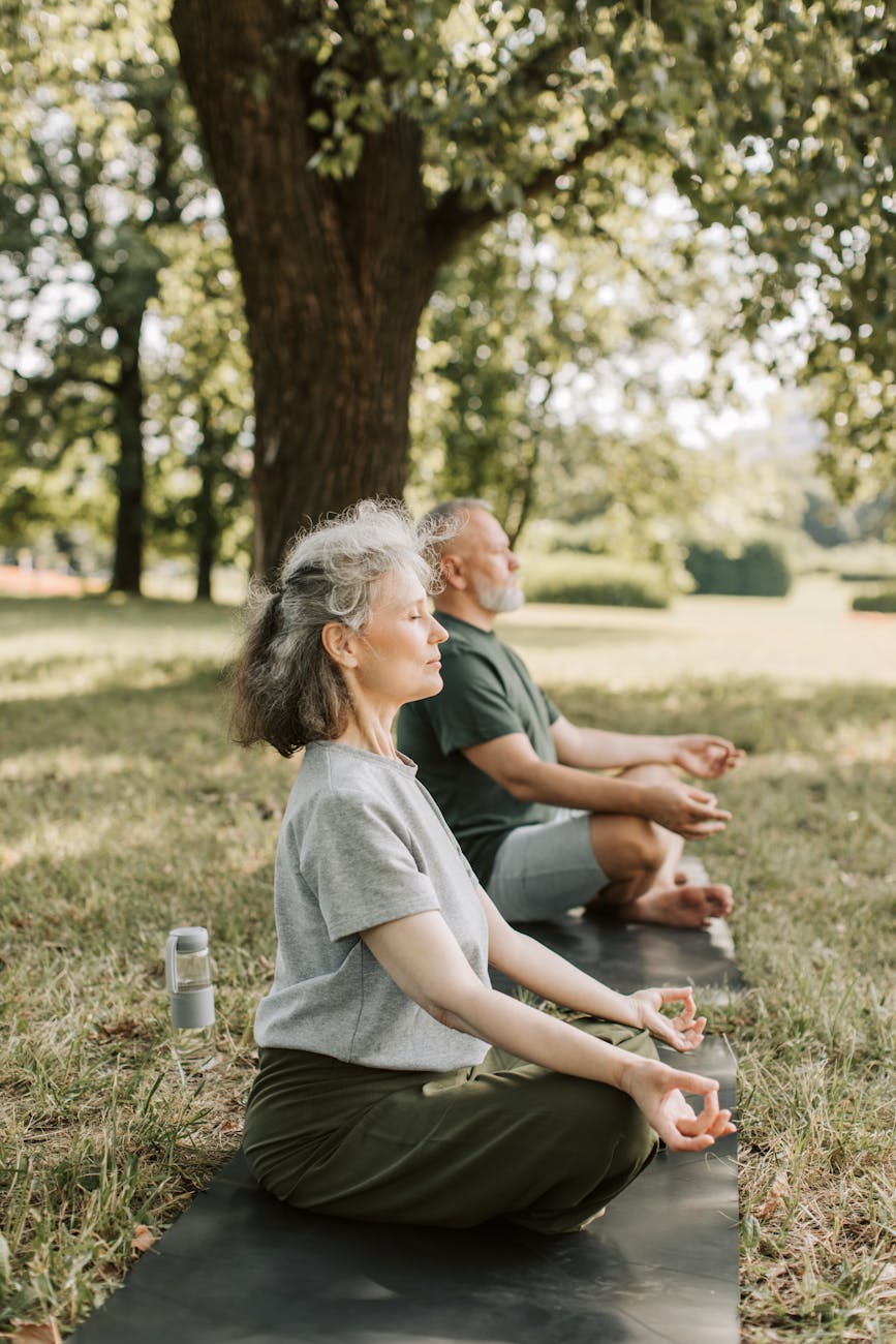 A man and a woman meditate outside on mats in the grass.