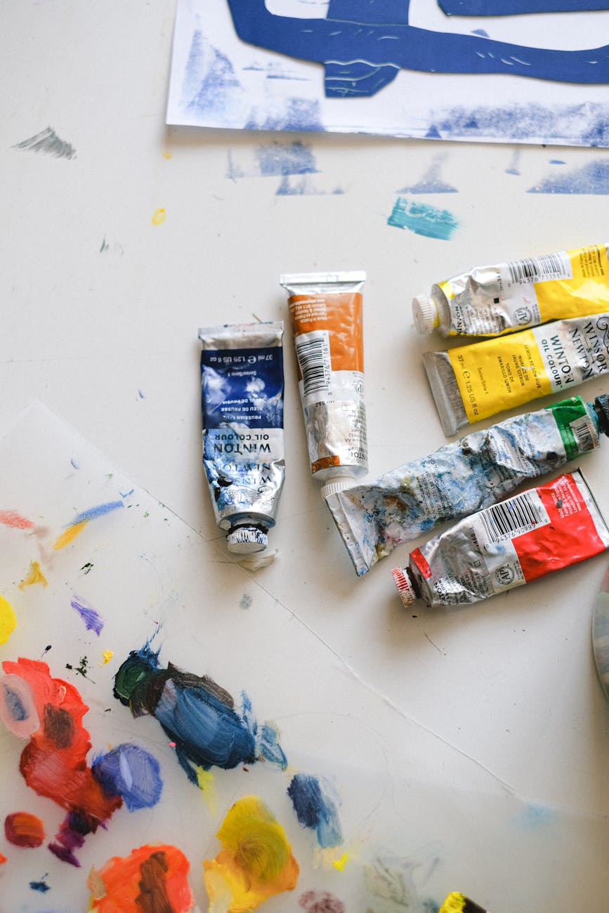 Paint tubes and red, blue, yellow, and orange paint strokes on a white canvas.