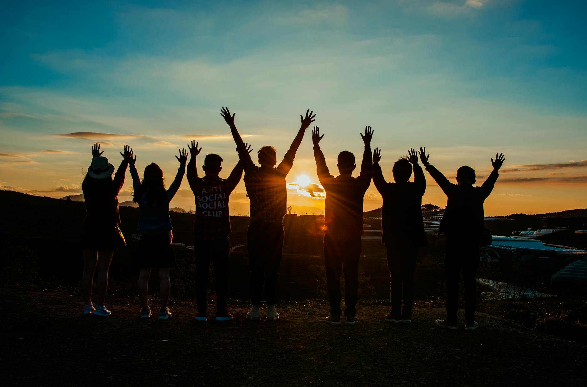 A group of people raise their arms as they watch the sunset.
