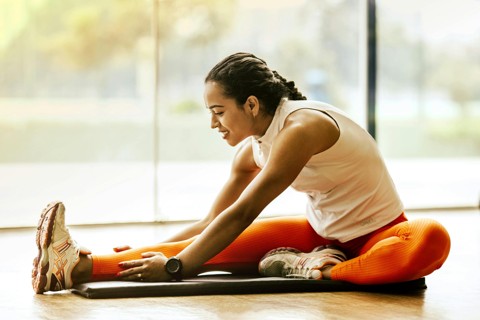 A woman wearing a beige top and orange leggings stretches on a mat.