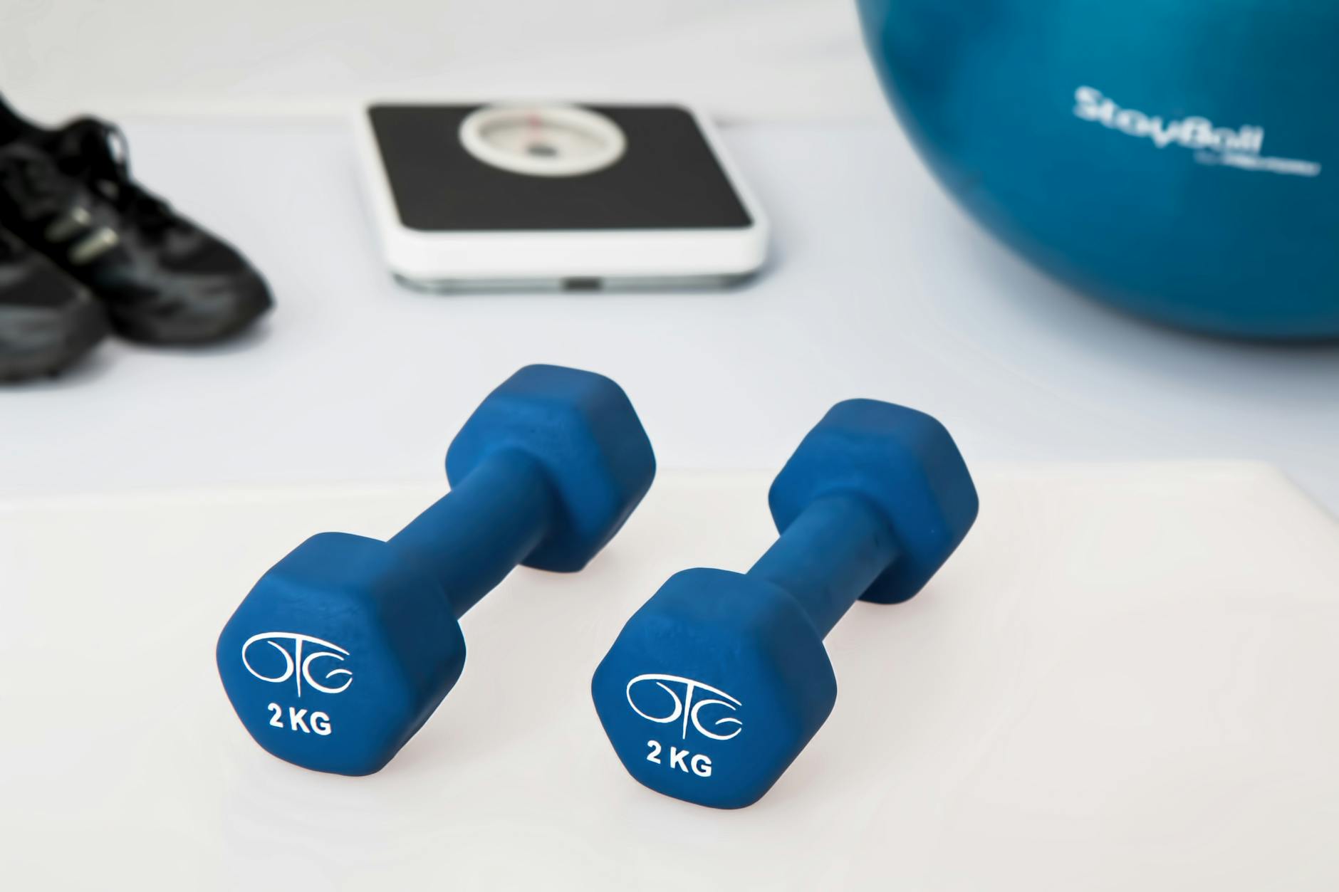 Two blue weights, a pair of gym shoes, a scale, and a blue exercise ball.